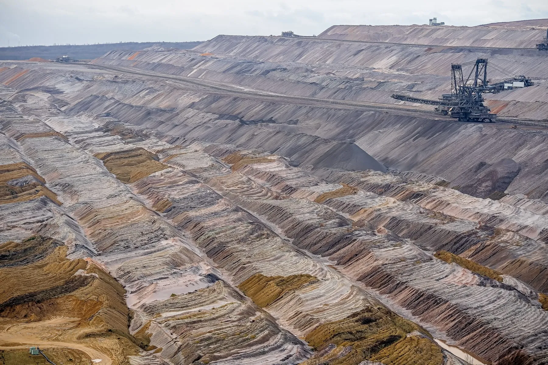 Aerial view of an open-pit mine, with excavation machinery working the terraced rock face.